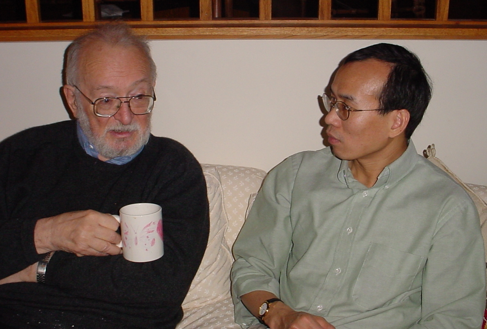 A candid photo of Zhi-Pei Liang and Paul Lauturbur sitting on a couch and talking; Lauturbur is holding a mug.