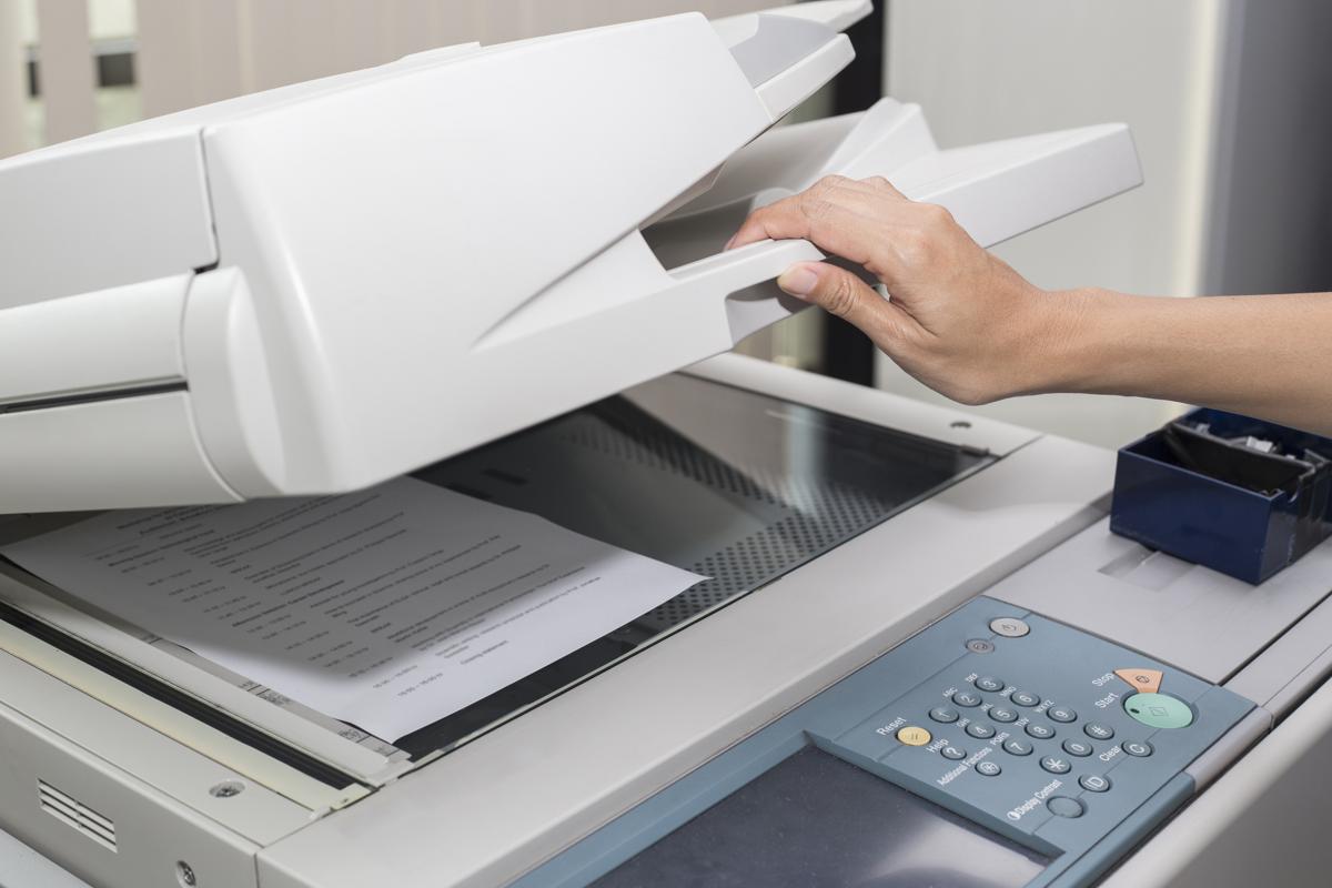 A woman's hand is closing a copier with a piece of paper on the glass