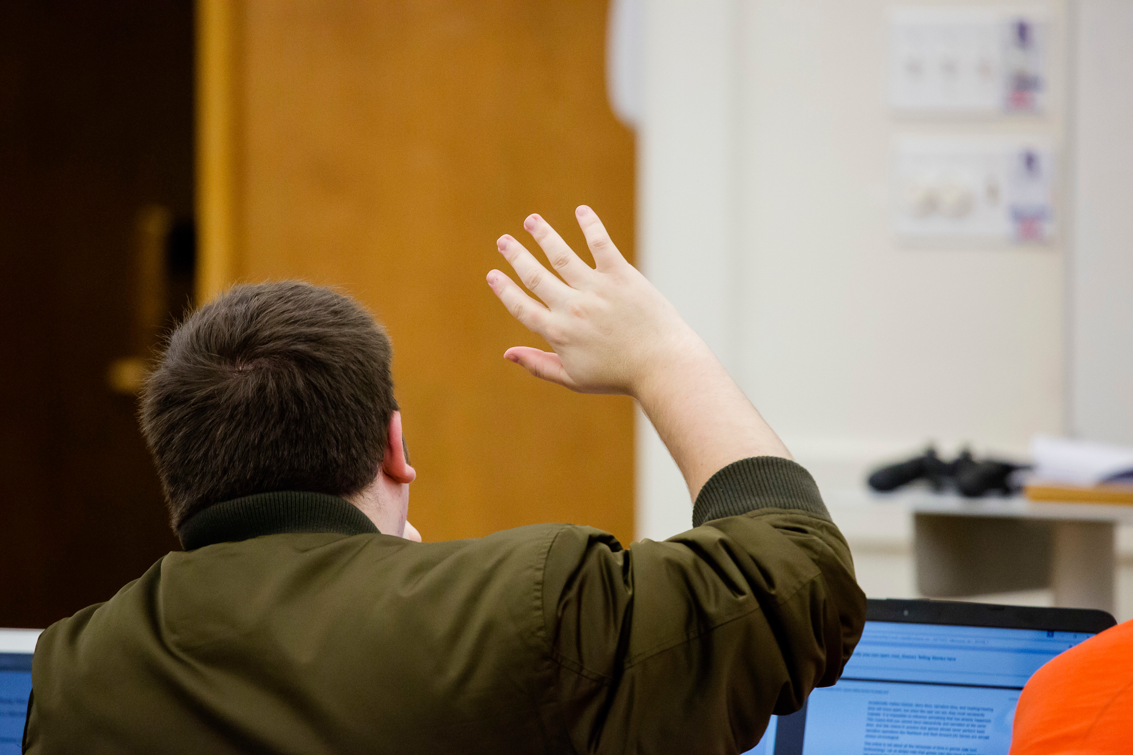 Male student raising a hand to ask a question in English 253 - topics in literature and new media.