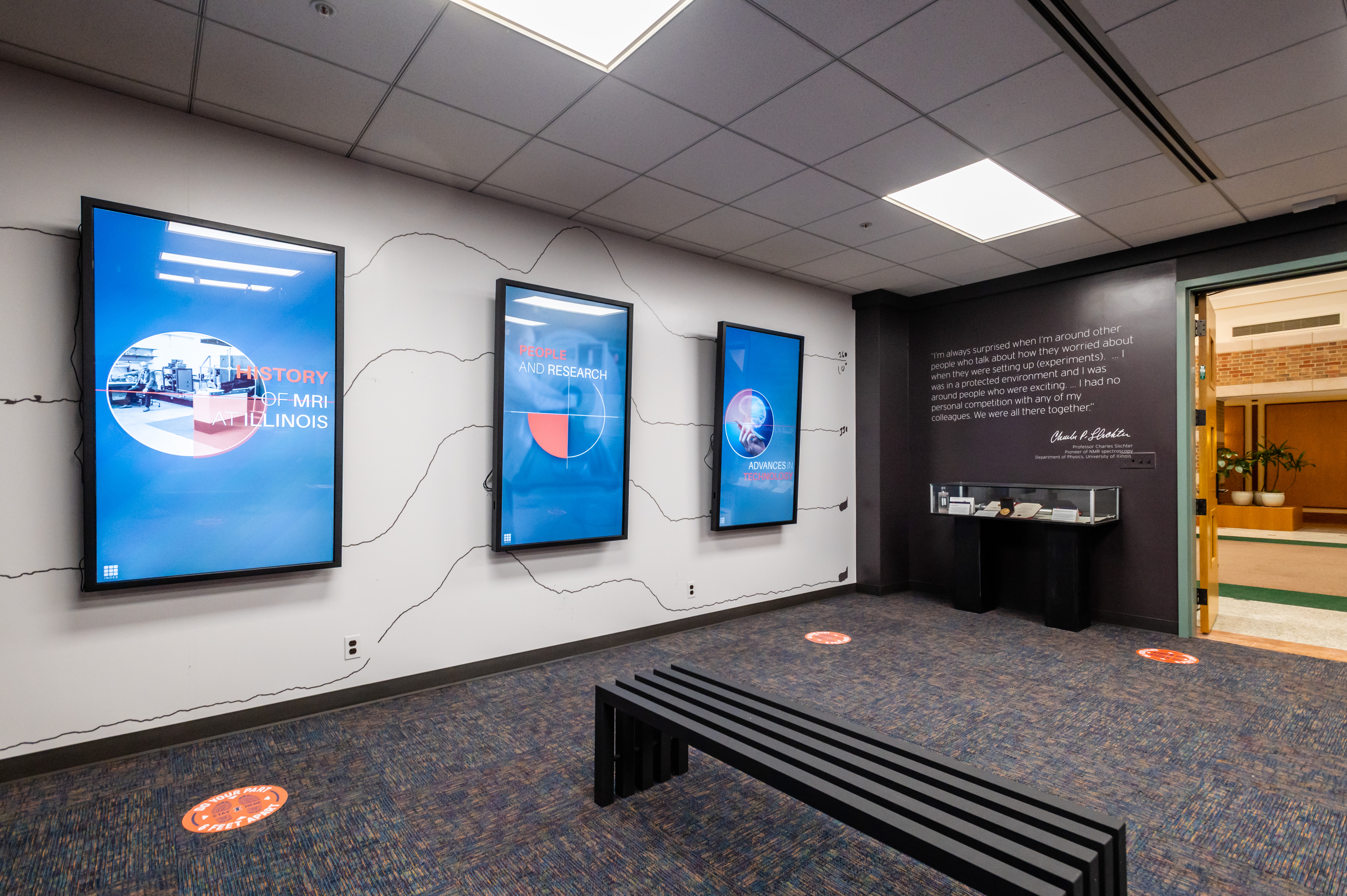 Three digital screens provide information about the history of MRI at Illinois in the Illinois MRI Exhibit.