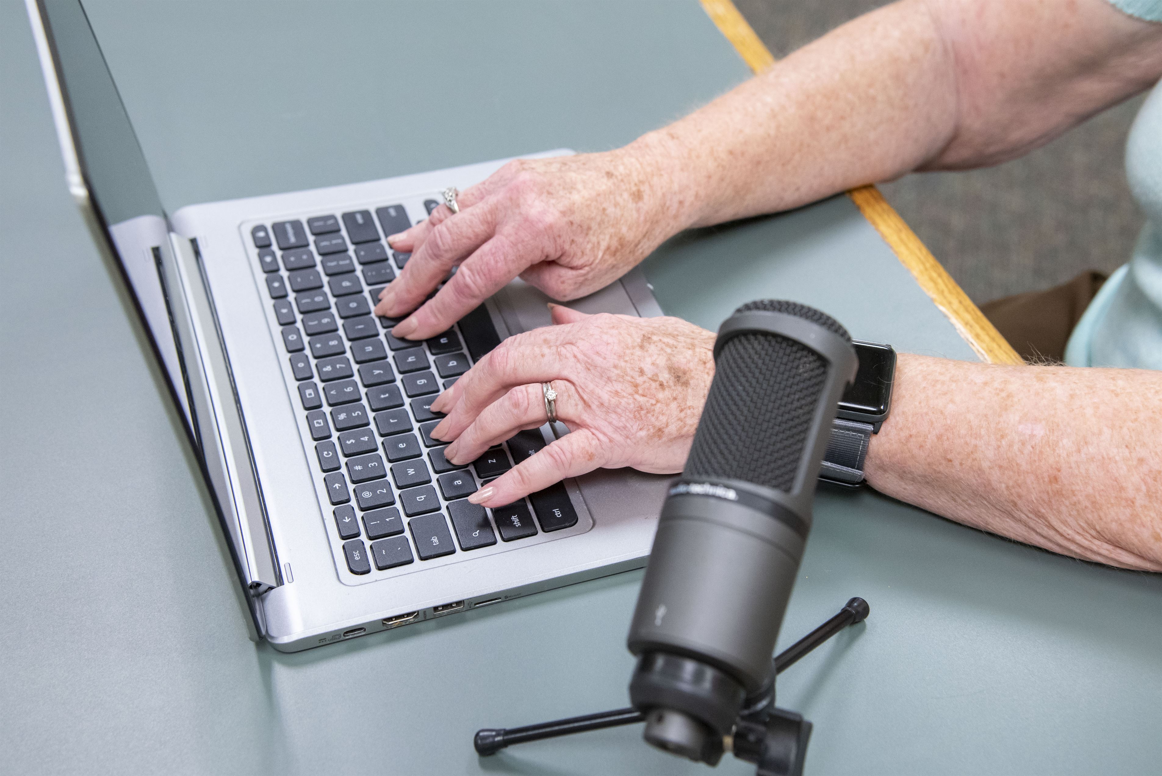 Closeup of hands typing on a laptop; microphone is in the foreground.