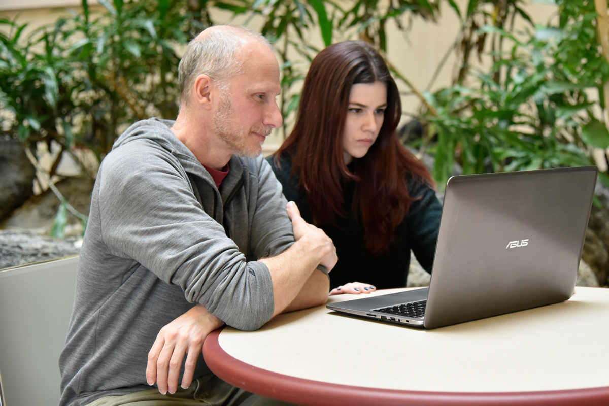 Benjamin-Siler-looking-at-computer-4239-WEB Prof. Aaron Benjamin with graduate student Jessica Siler review notes on her laptop in the atrium of the Psychology Building.