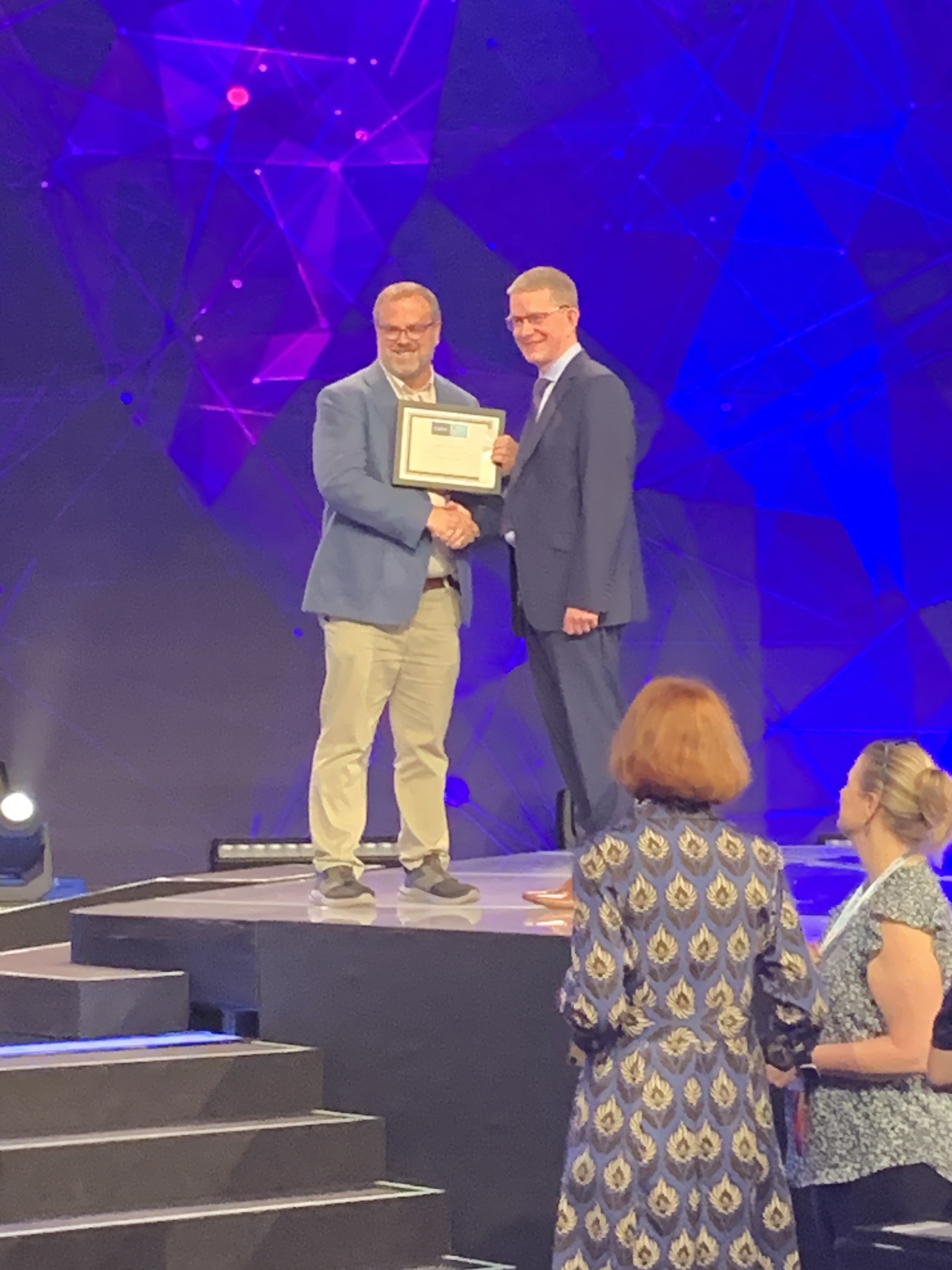 Sutton on a stage, holding a certificate.