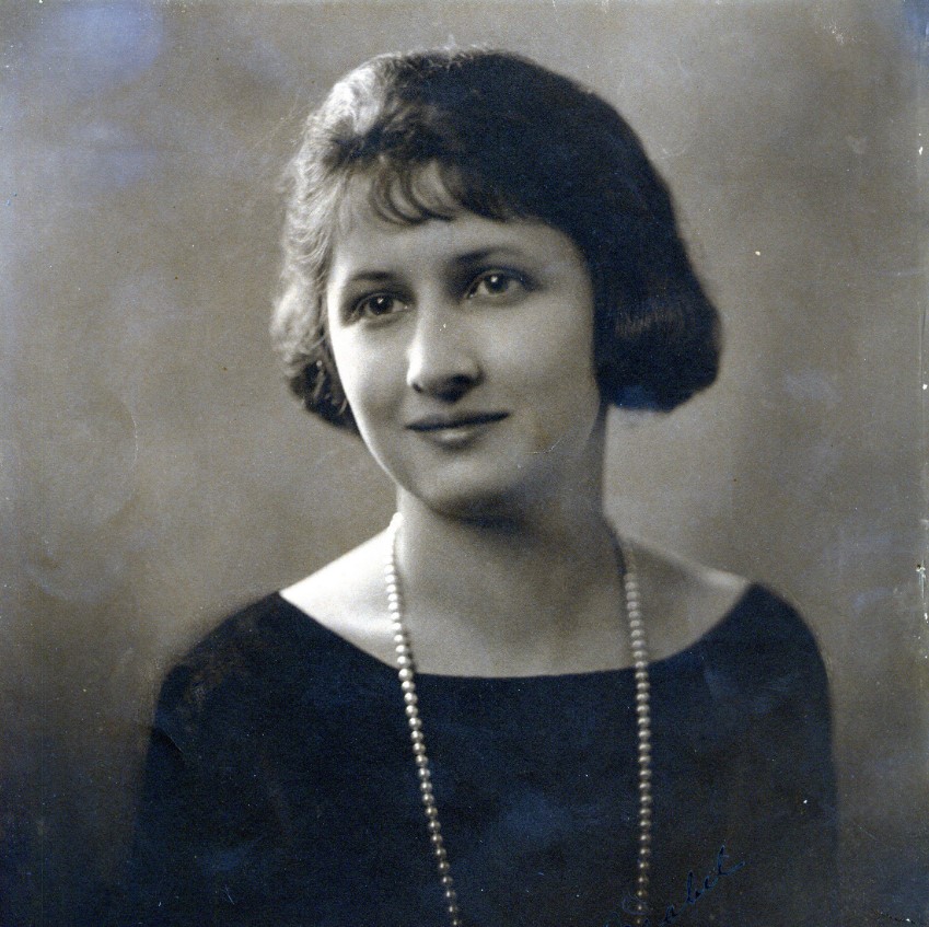 A black-and-white portrait-style photo of Mabel Beckman. She wears a simple black shirt and a pearl necklace, and her gaze is slightly to the left of the camera.