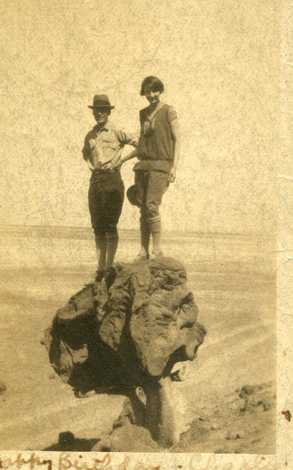A yellowing photo of Arnold and Mabel Beckman standing on a large boulder in an otherwise barren landscape. Mabel is notably wearing trousers.