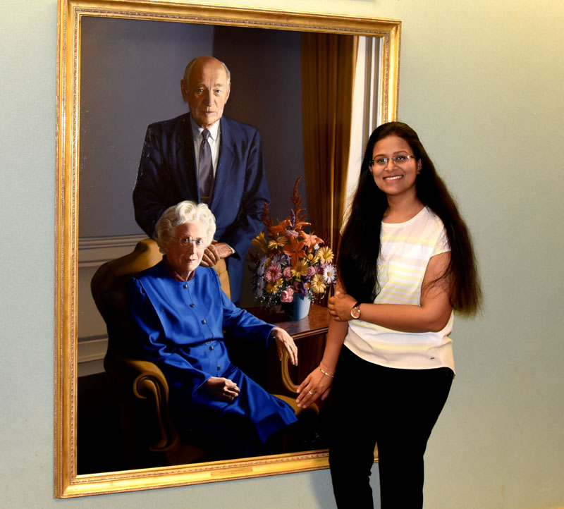 Shachi Mittal stands beside a portrait of Arnold and Mabel Beckman, reenacting the route she would take as a postdoctoral researcher to find inspiration from years past.