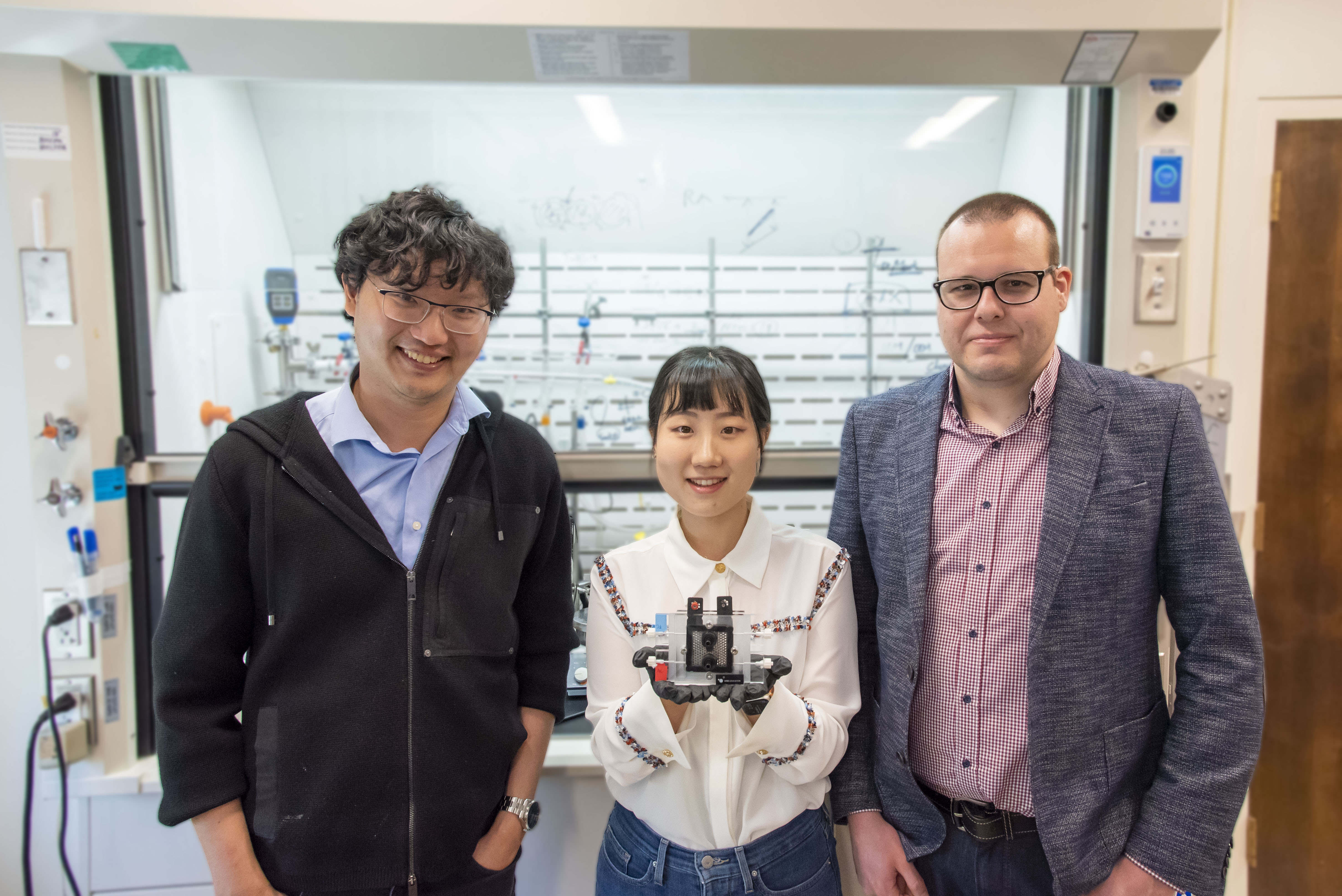 Three researchers in a lab, with the center researcher holding a small device in outstretched hands.