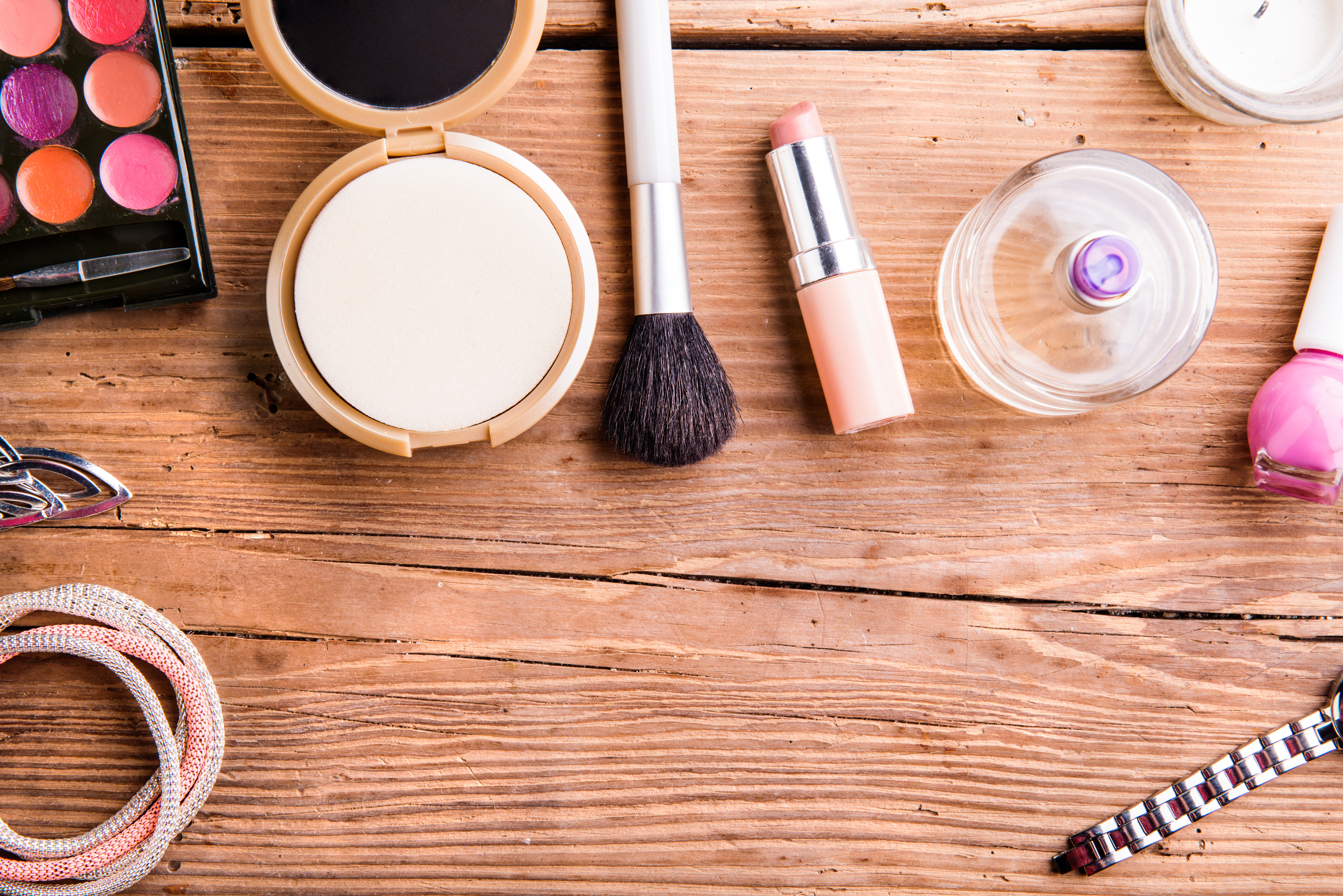 Various make up products, including lipstick, nail polish, and makeup brushes, laid flat on a wooden tabletop.