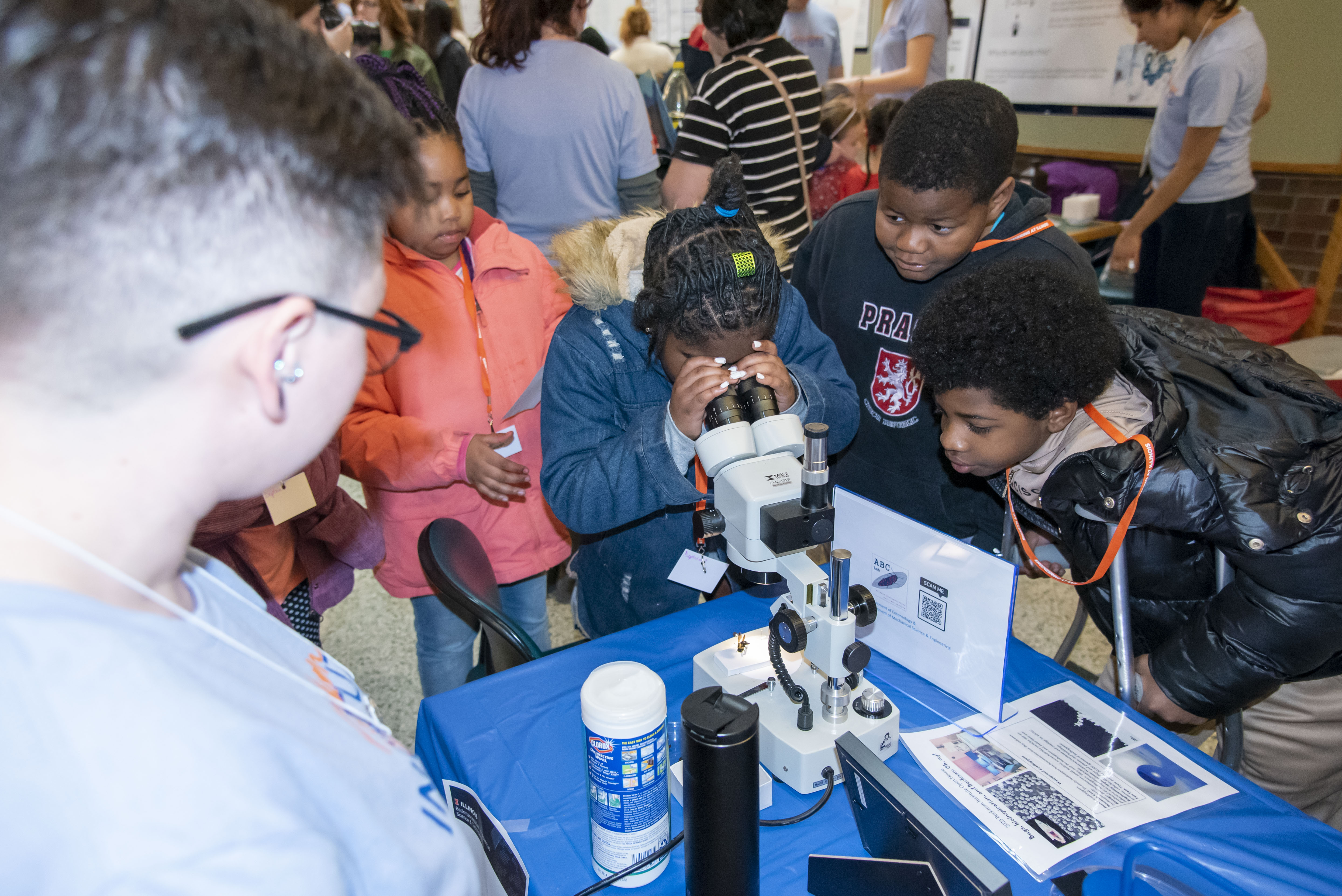 A student looks through a microscope at the Beckman Institute Open House 2023 while her peers look on.