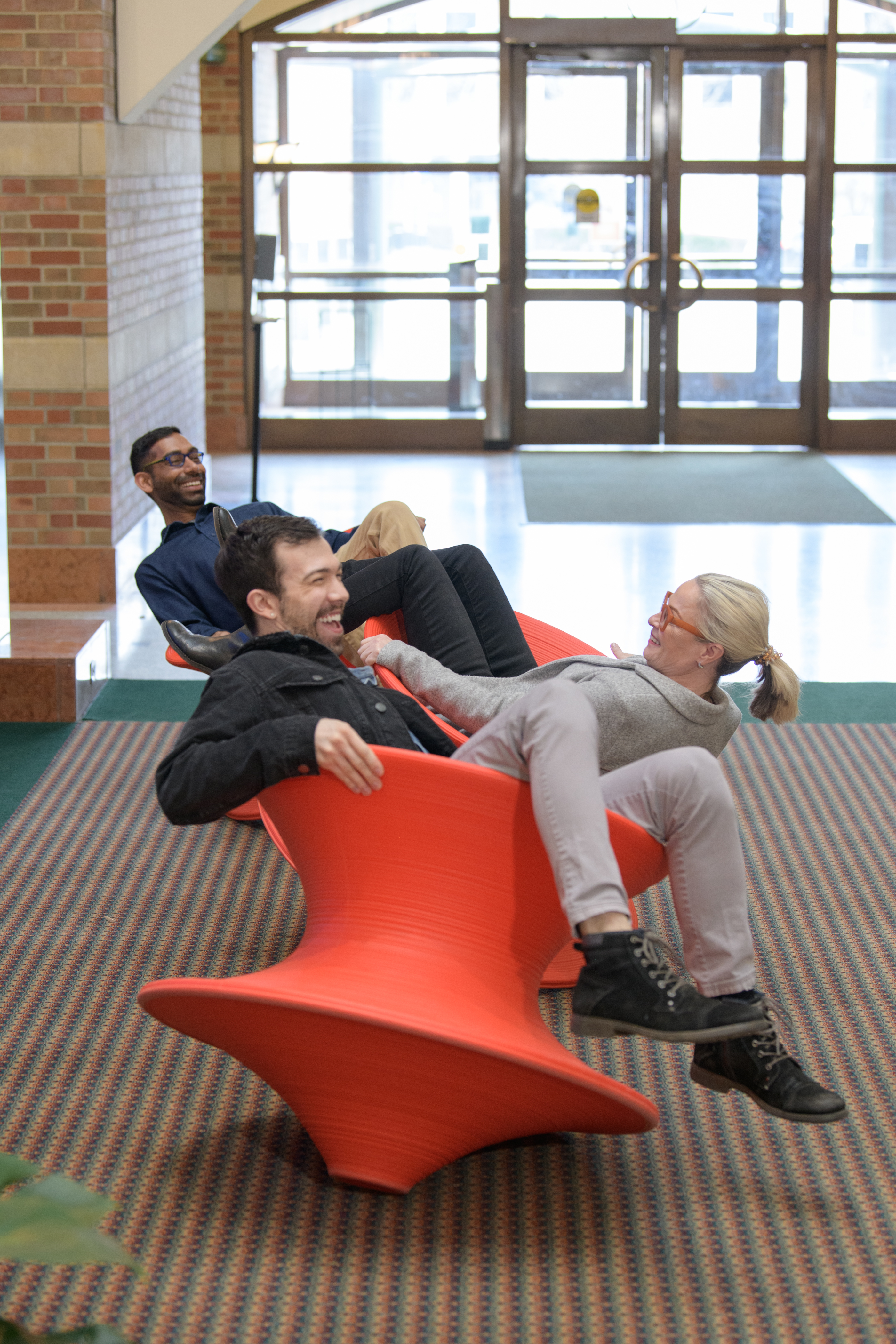 Three individuals, including Deana McDonagh, joyfully spin on the Spun Chairs in Beckman's remodeled atrium.