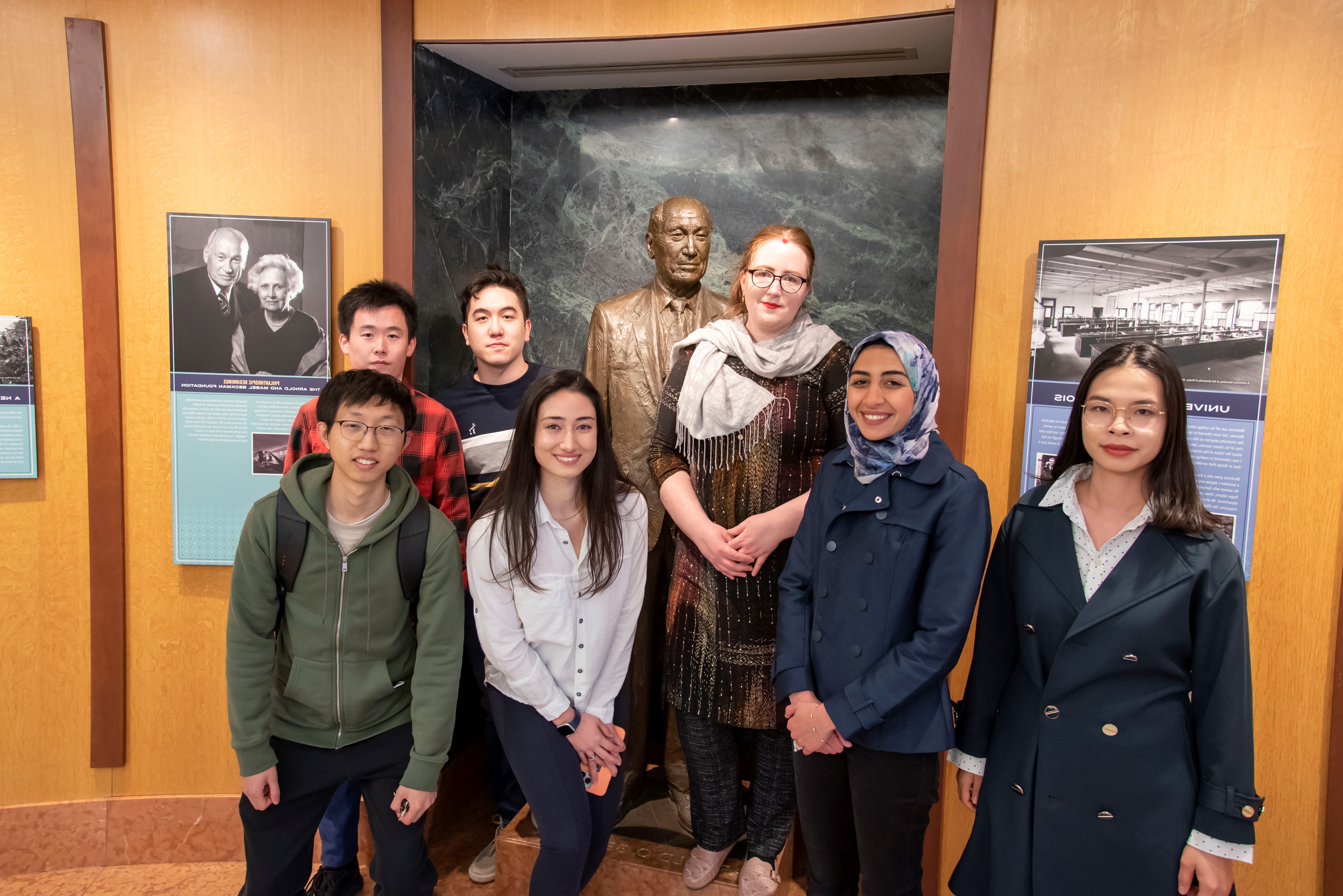 Students comprising the 2022 Beckman Institute Graduate Fellows cohort pose for a photo in front of the statue of Arnold O. Beckman in the institute's rotunda entrance.