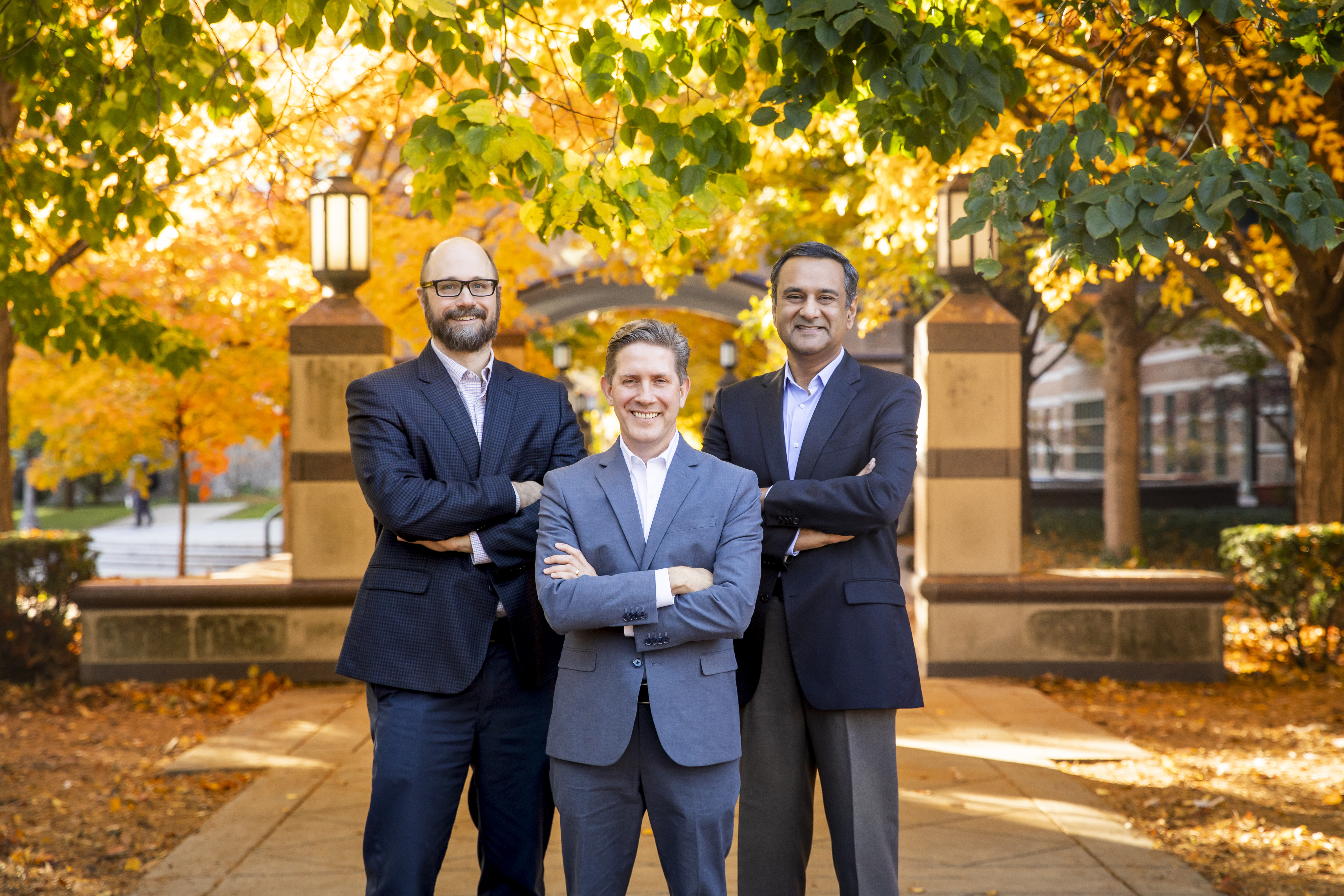 Three male researchers pose outside of the Beckman Institute, illuminated by the brilliant yellow and gold colors of fall leaves.