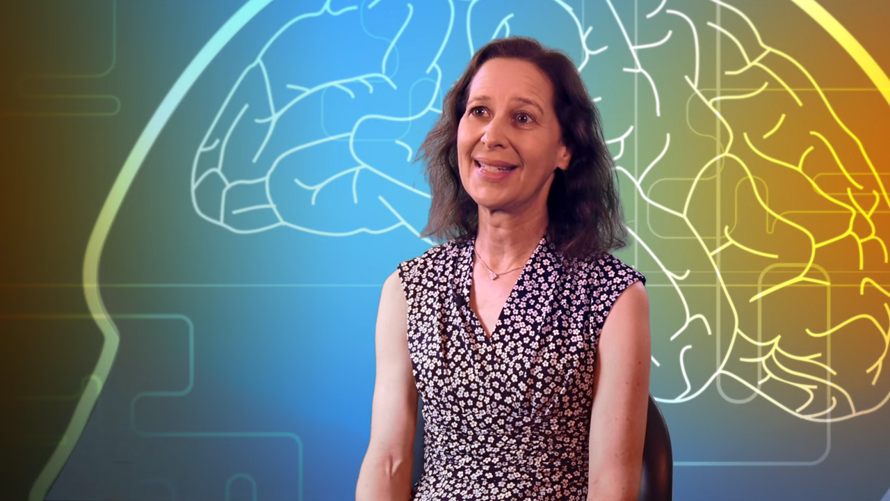 Karen Rudolph sits in front of a backdrop patterned with a graphic of a brain