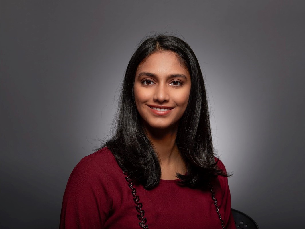 a smiling woman with long black hair who is wearing a burgundy blouse