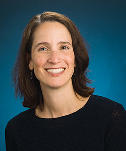 Nancy McElwain, a woman with dark brown shoulder-length hair wearing a black shirt and smiling.