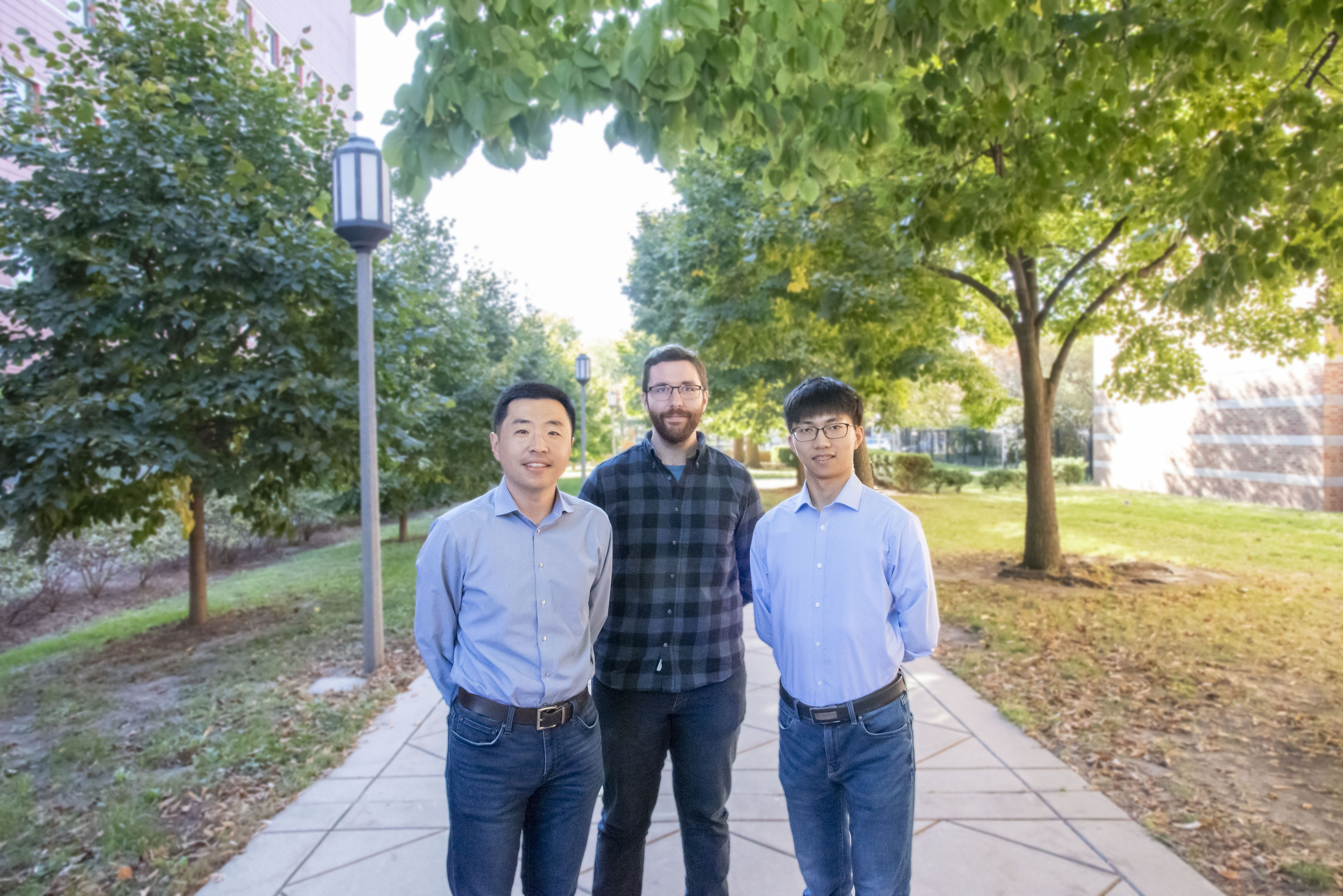 Pengfei Song, Matthew Lowerison, and Zhijie Dong stand on the pathway in front of the Beckman Institute.