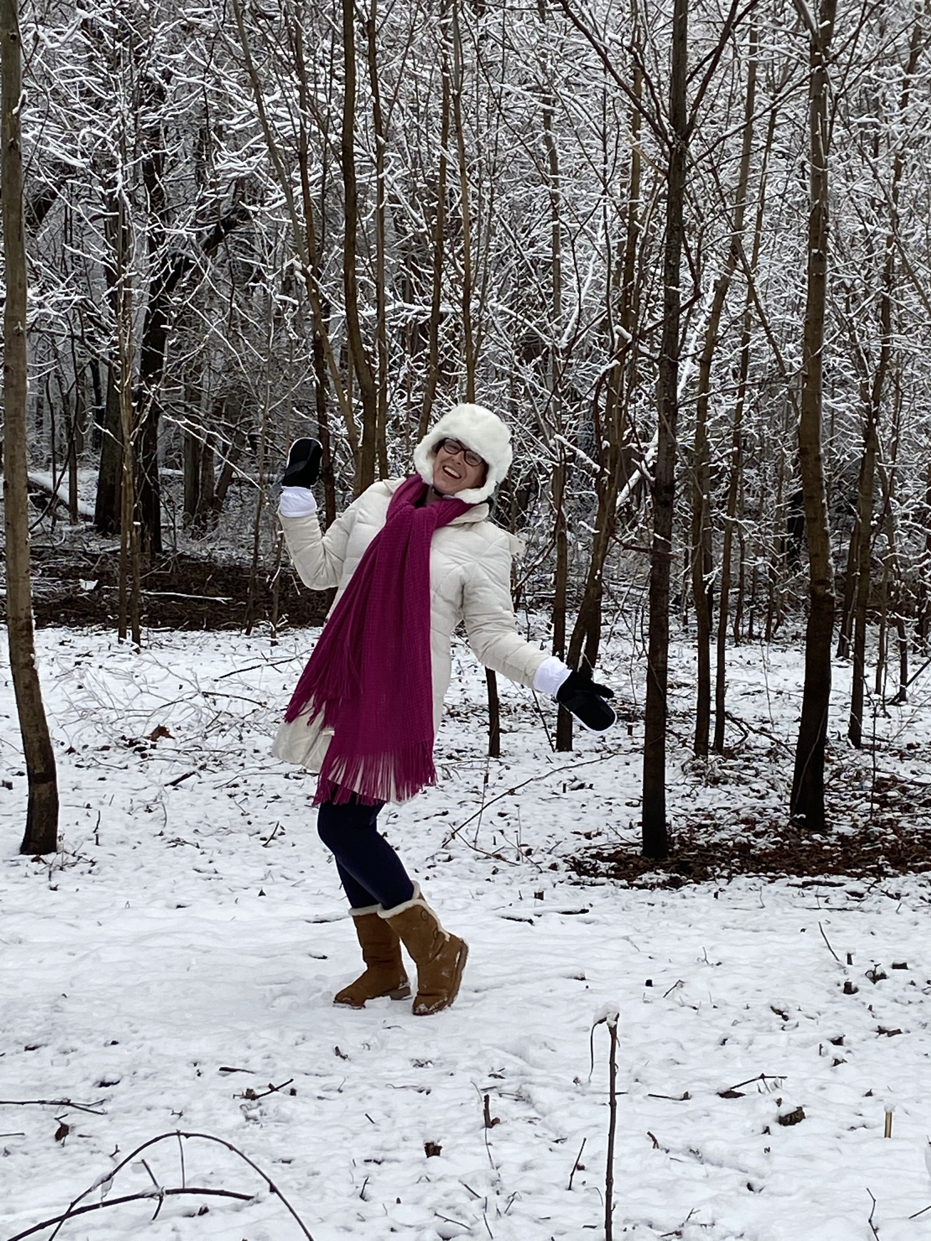 Dressed in cold-weather clothing, including winter boots and a long magenta scarf, Shawna Graddy enjoys a snowy forest landscape.