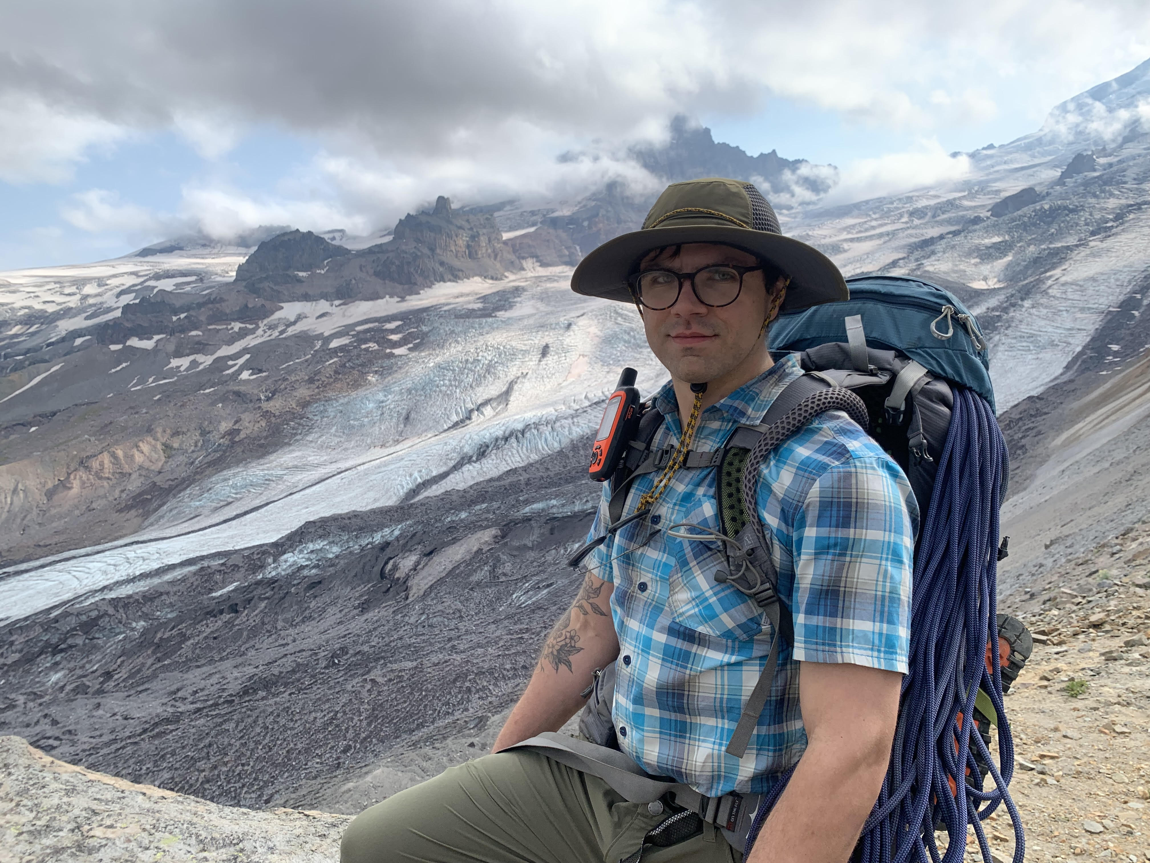 Tim Trinklein, dressed in hiking gear, poses with a mountain view behind him.