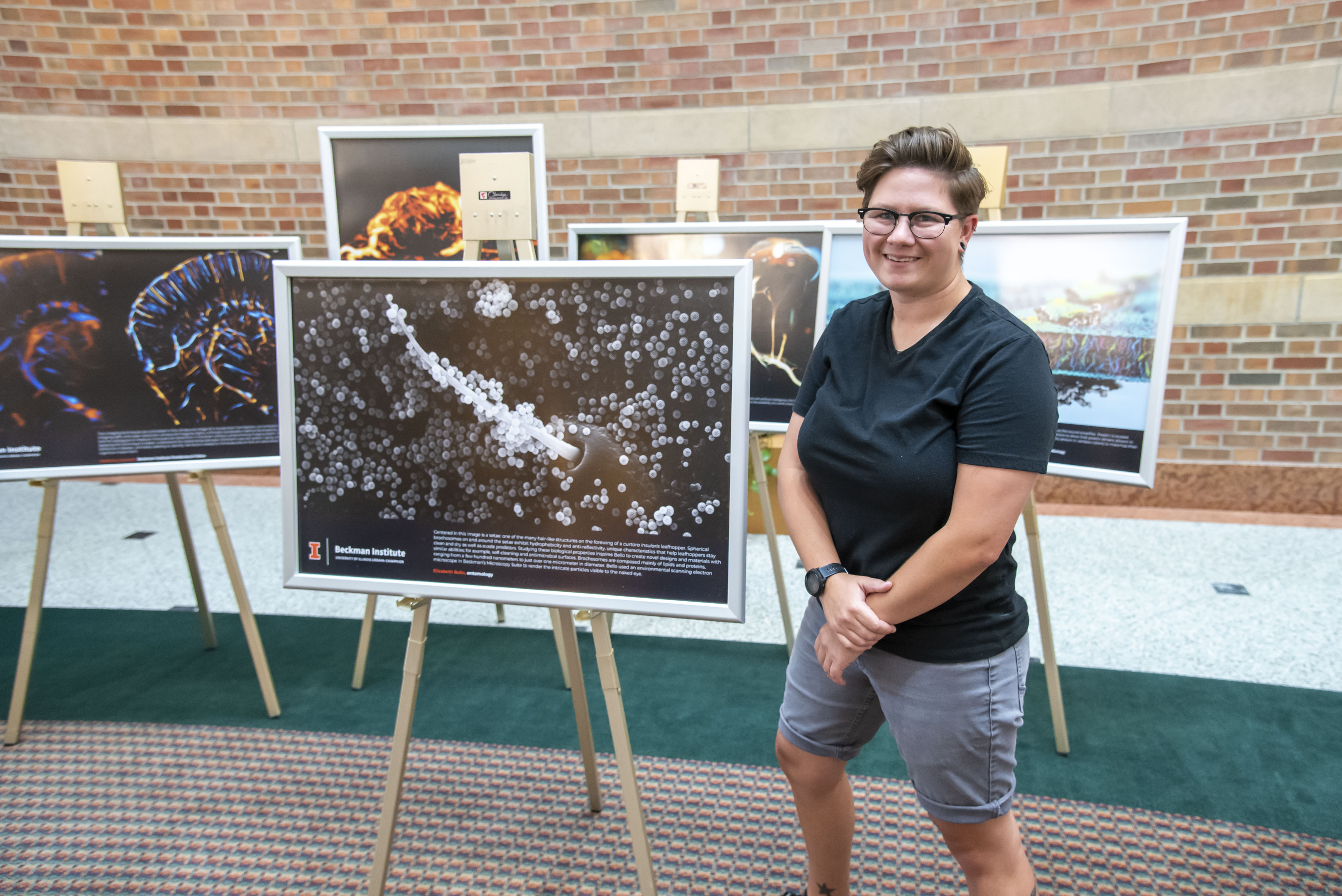 Student researcher Elizabeth Bello stands beside her framed research image, mounted on an easel in the Beckman Atrium.