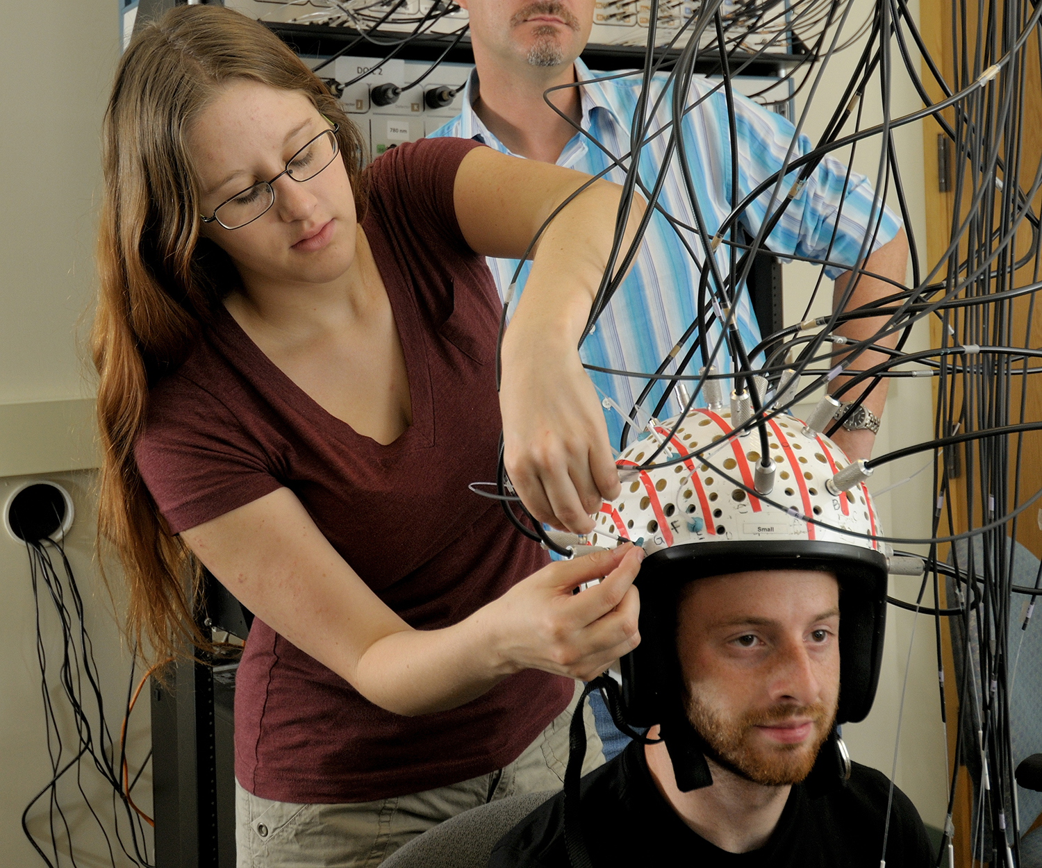 A researcher sets up diffuse optical imaging to measure the brain, which means attaching wires to a cap