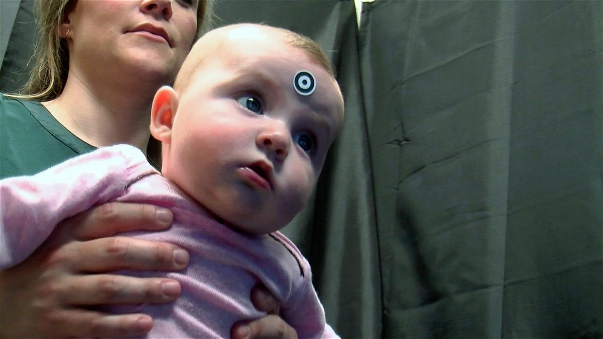 A baby, wearing a eye-tracking sticker that looks like a target between her eyes, looks at a screen as a part of IKIDS research.