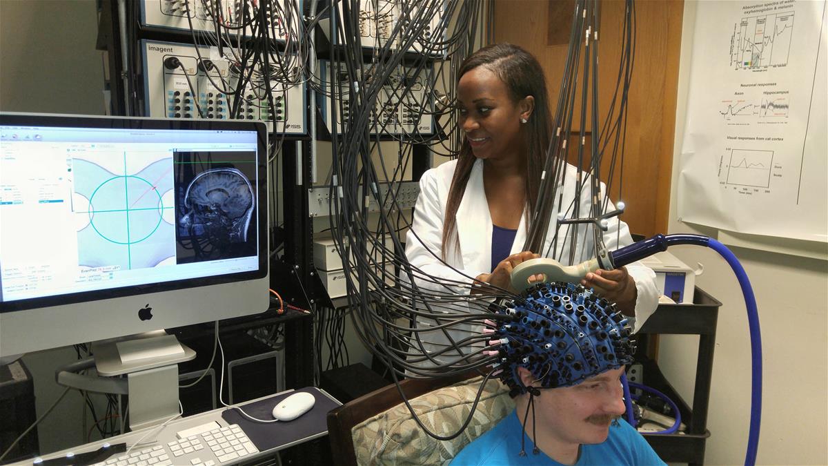 A researcher hooks a subject up to an optical brain imaging took, which looks like a cap connected to many wires.