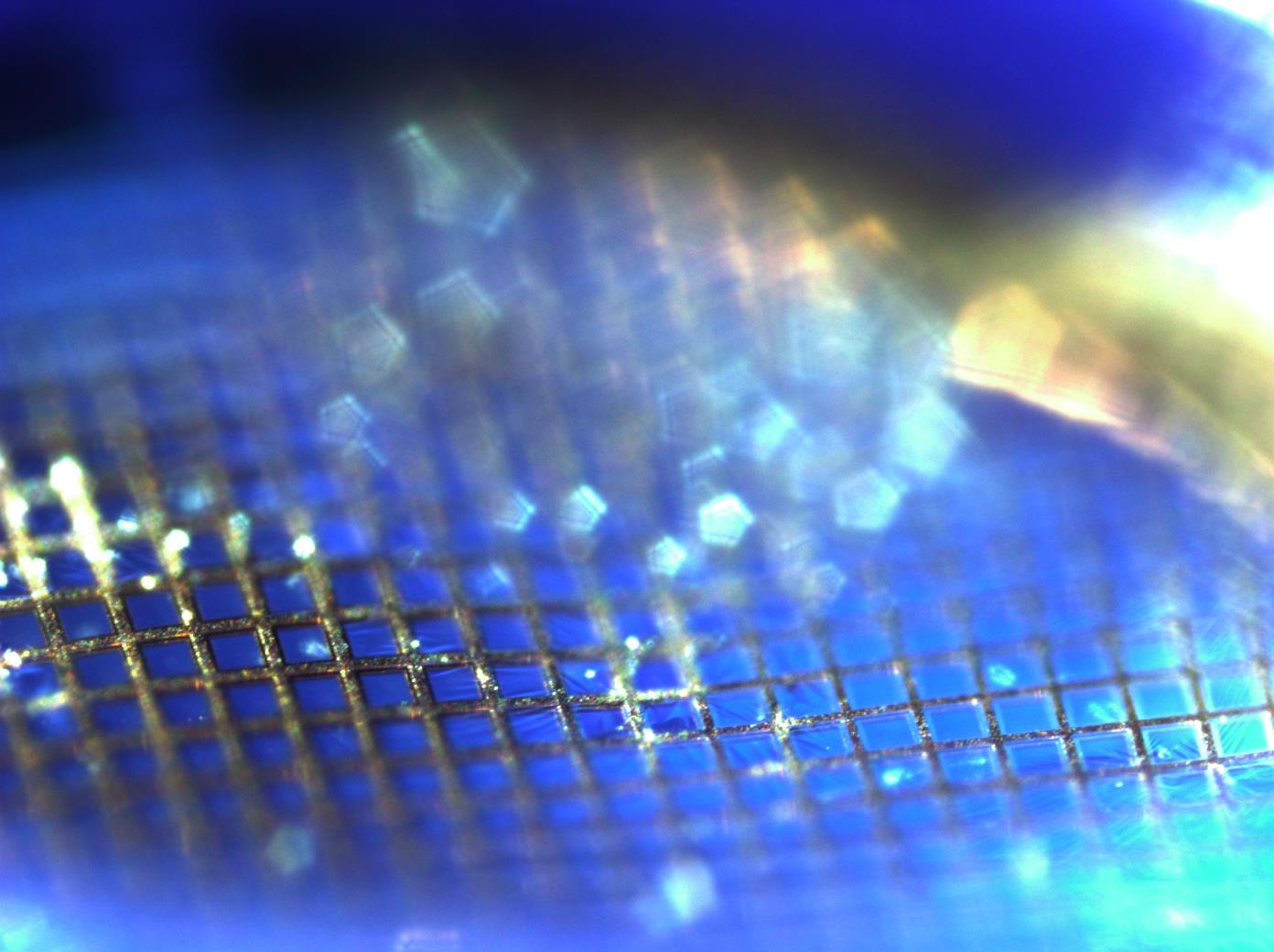 Metal nanoparticles, magnified to 100 times their original size, appear as floating pentagons due to the angled, intensely focused light on the pointed upper edges of the metal grid lines.